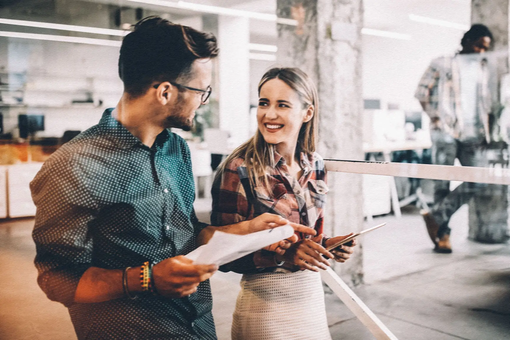 A man and a woman chat in a professional business environment while standing.
